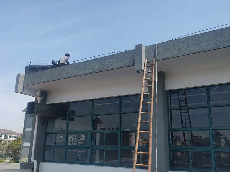 學校屋頂防水：屋頂做防水前，要先對需要防水施工的屋頂基層進行清潔，因為很多防水施工中要避免一些雜物、塵土等，打掃干凈了更有利于防水施工效果。屋頂防水施工就與室內防水施工差不多，室內的地漏、水管位置等都要重點涂刷，而屋頂中的水落口、女兒墻、檐口、陰陽角等位置也要先進行針對性的施工，也被稱為附加層施工。屋頂施工防水需要不少材料，特別是防水用的改性瀝青卷材、防水涂料等等，先對基層鋪貼一層防水卷材，其厚度要符合要求，尺寸根據屋頂面積進行裁剪。卷材一般歐式用熱熔的方式來鋪貼，也就是需要借助火焰噴槍來加熱進行滾鋪、粘貼，卷材從檐口處與屋脊平行的方向由下而上進行鋪貼。卷材的各個搭接處都要用噴槍來加熱粘結牢固，并且在邊緣末端收頭處要用密封膏來嵌填嚴密好才行。卷材鋪貼好后，要再一次進行屋頂清潔，保障干凈、干燥的施工環境，這時候就可以進行第一層的防水涂料刷涂了，第一遍一定要涂滿，不能出現遺漏、裂紋、氣泡、黏合不牢固等現象。