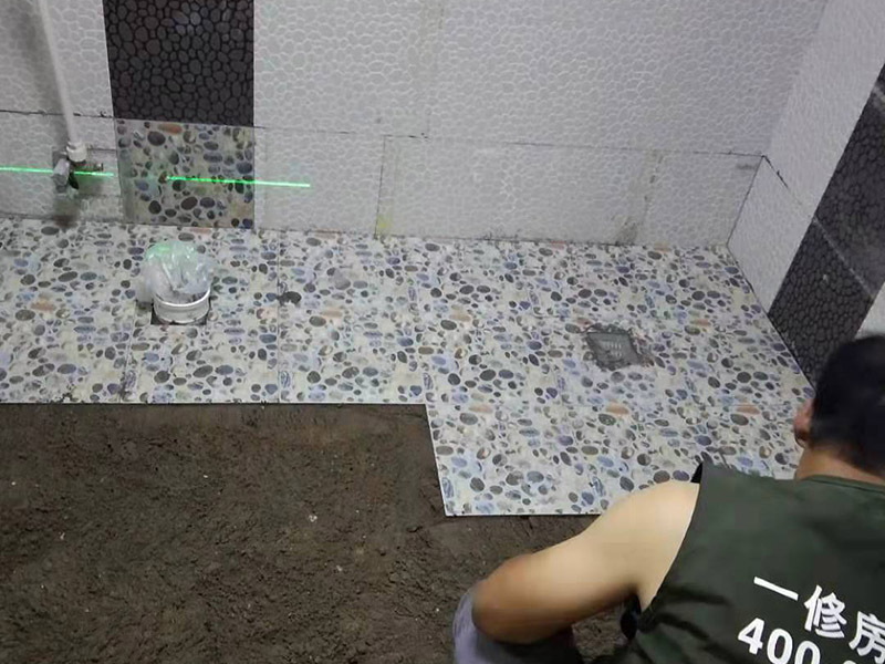 衛(wèi)生間地面花磚鋪貼:找平，就是在鋪仿古磚前，對(duì)鋪貼物表面進(jìn)行處理，如地面、內(nèi)墻面、外墻面等，消除表面附著的污物，并灑水進(jìn)行滋潤，然后用水泥沙混合找平，通常使用灰鏟在表面不停的涂抹使水泥地面保持大致水平，一定要等到水泥沙混合物完全干爽后再行鋪貼。用一段較長的細(xì)線，根據(jù)確定的鋪貼方式，在線上涂上顏色或白灰，然后在找平的地面上畫出仿古磚的位置及磚縫的參考線。 將亞光磚置入清水中浸泡，使瓷磚充分吸收水分，以不冒出氣泡為準(zhǔn)，防止干燥瓷磚在裝修完成后再次吸水而導(dǎo)致磚體變形。取出浸泡好的瓷磚，抹干水漬，在找平層上噴灑足夠的水，然后在磚背面均勻抹上水泥沙漿，沙漿厚度5~6cm為宜，鋪貼大規(guī)格亞光磚時(shí)適當(dāng)加厚；隨即將磚貼上，用木錘輕輕拍牢平整，避免空鼓，并隨時(shí)用直尺找平。